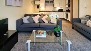 A modern living room with a grey sofa, a coffee table with books and a vase, and a kitchen in the background. - Lovely One Bed Apartment in Hip End of Temple Bar (Dublin 8)