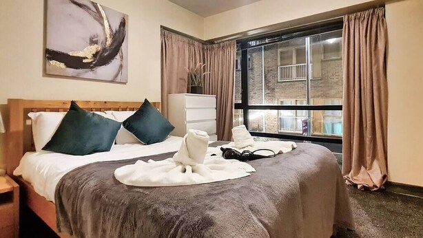A hotel room with a bed, a nightstand, a dresser, and a window with curtains. - Lovely One Bed Apartment in Hip End of Temple Bar (Dublin 8)