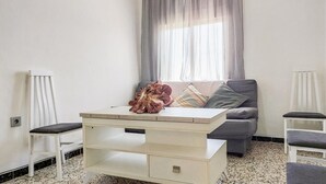 Een kamer met een witte bank, een witte stoel, een tafeltje met een decoratief object en een raam met dunne gordijnen.