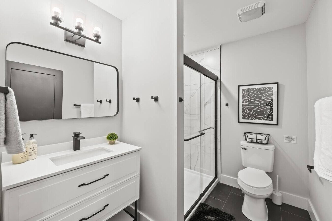 A modern bathroom with a white vanity, a large mirror, a shower with a glass door, and a toilet.