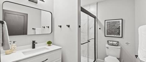 A modern bathroom with a white vanity, a large mirror, a shower with a glass door, and a toilet.