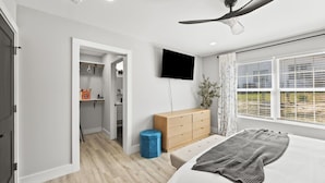 Une chambre à coucher comprenant un lit, un ventilateur de plafond, une télévision, une fenêtre avec des stores et un placard avec des étagères.