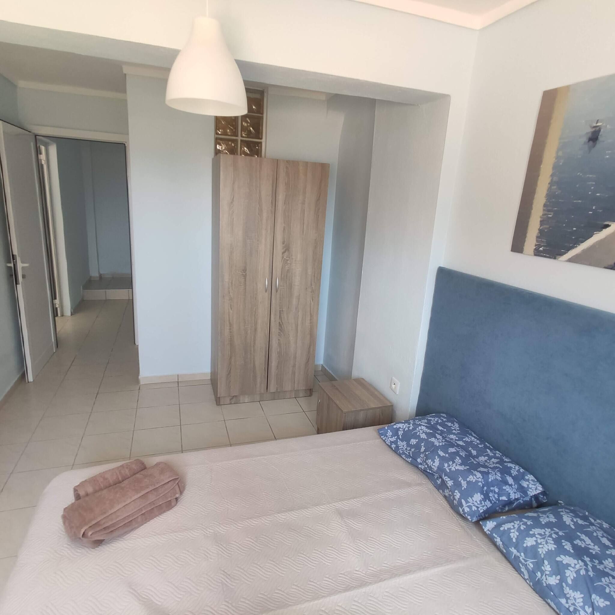 A bedroom with a bed, a wardrobe, a hanging light, and a painting on the wall.