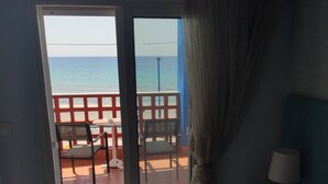 A hotel room with a bed, a nightstand, a lamp, and a view of the sea through a sliding door.
