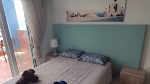 A hotel room with a bed, a TV mounted on the wall, a painting above the bed, and a view of the outside through a window.