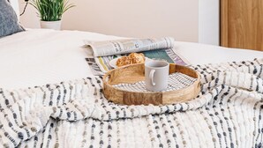 A neatly arranged bedroom with a bed, a bedside table with a lamp, framed artwork, a potted plant, and a tray with a mug and pastries. - Central Chester: Cozy and Modern Flat (Chester)