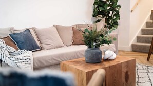 Een woonkamer met een bank, een salontafel, een potplant en een trap.