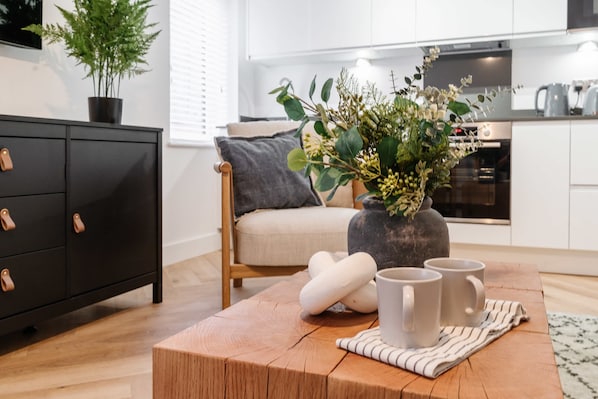 Un salon moderne avec une table basse en bois, un meuble noir, un canapé gris et une plante en pot.
