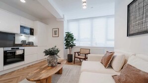 Ett modernt kök med inbyggda vitvaror, ett träbord, en soffa och ett stort fönster med persienner.