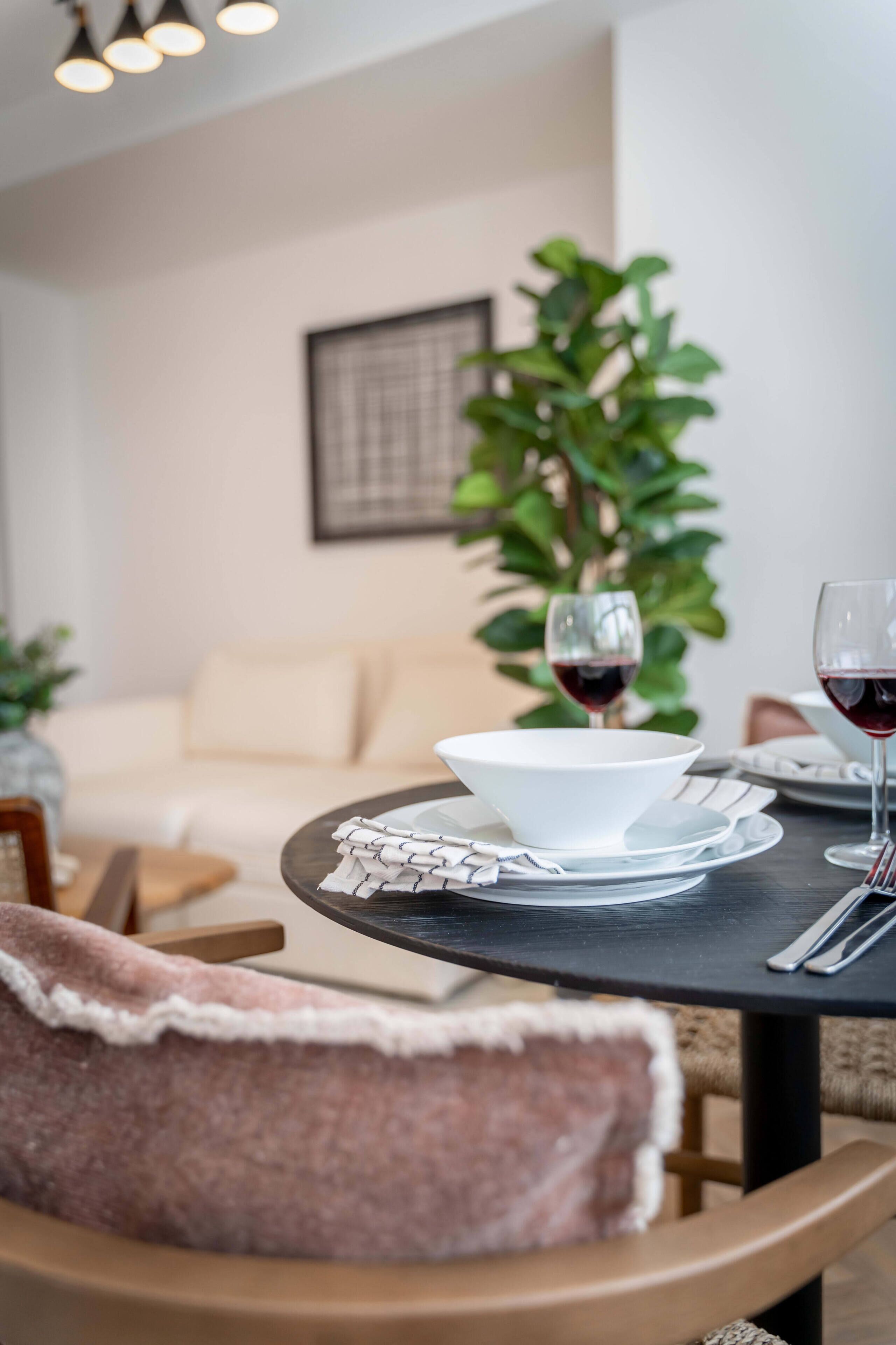 A dining table with a bowl, wine glasses, and cutlery, a sofa, and a potted plant in a modern interior.
