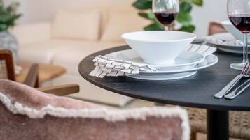 A dining table with a bowl, wine glasses, and cutlery, a sofa, and a potted plant in a modern interior.