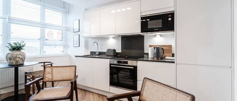 A modern kitchen with white cabinets, a black microwave, and a dining area with wicker chairs.