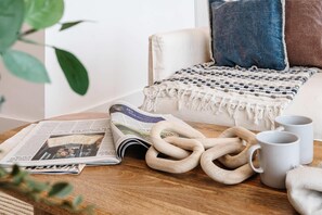 Un rincón acogedor para leer con una silla, una manta, un periódico, dos anillos de madera y dos tazas blancas.