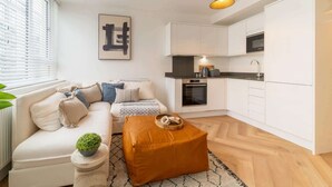 A compact living space with a sofa, ottoman, and kitchenette. - Stylish Chester City Apartment (Chester)