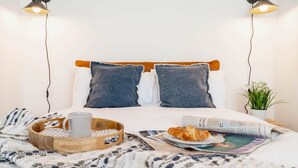 A neatly made bed with a wooden headboard, a tray with a mug and croissant, a plant, and a newspaper. - Stylish Chester City Apartment (Chester)