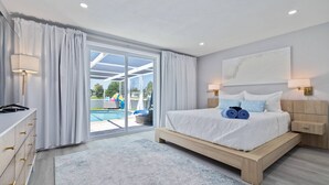 A modern bedroom with a large bed, a wooden dresser, and a view of a swimming pool through glass doors. - Luxury 3BR Home w/ Heated Pool, Outdoor TV, Bikes & BBQ – Perfect for Families with Modern Kitchen! (Port Richey)