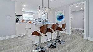 A modern kitchen with white cabinetry, a central island, and three bar stools with a unique design. - Luxury 3BR Home w/ Heated Pool, Outdoor TV, Bikes & BBQ – Perfect for Families with Modern Kitchen! (Port Richey)