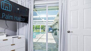 A modern hotel room with a large sliding glass door leading to a pool area. - Luxury 3BR Home w/ Heated Pool, Outdoor TV, Bikes & BBQ – Perfect for Families with Modern Kitchen! (Port Richey)