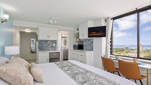 Habitación de hotel con cama, escritorio con dos sillas, televisión, vista de la ciudad y kitchenette.