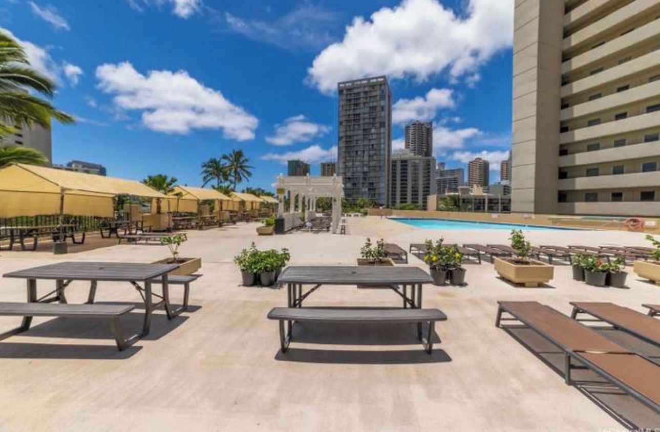 A rooftop pool area with picnic tables, lounge chairs, and a view of the city skyline.