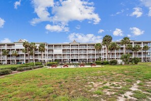 A multi-story hotel with balconies, palm trees, and a grassy lawn with picnic tables.