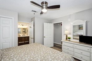 A bedroom with a bed, dresser, TV, and a ceiling fan.