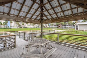 A covered outdoor area with a wooden deck, a hexagonal table, and a view of a residential building complex in the background.