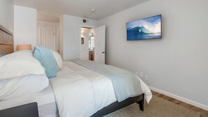 Een slaapkamer met een bed, een schilderij van een golf en een deur naar een badkamer.