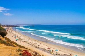 A beach with a pier extending into the ocean, sandy shores, and people enjoying the beach.
