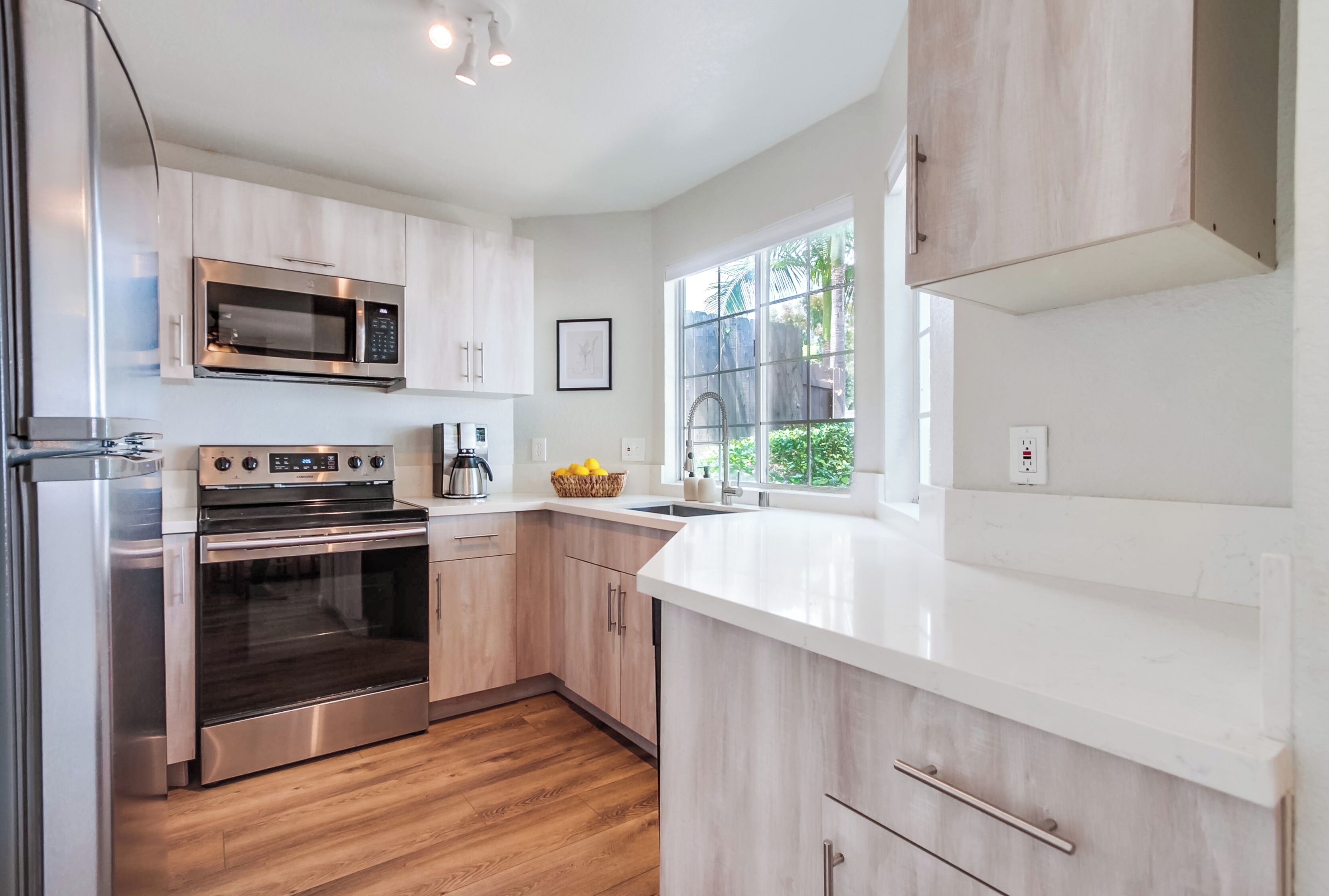 A modern kitchen with stainless steel appliances, wooden cabinets, and a large window providing natural light.