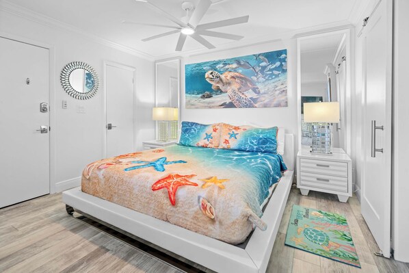 Una camera da letto con un letto, una ventola a soffitto, un quadro raffigurante un'tartaruga marina, un comodino e un tappeto.