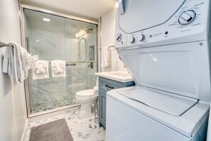 Un bagno moderno con cabina doccia in vetro, un water bianco e una lavatrice e asciugatrice affiancate.