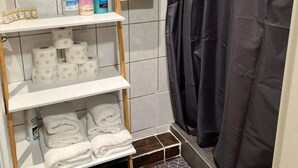A bathroom with a shelf holding toiletries, toilet paper, and towels. - Stadtnahe Wohnung mit Küche - Ideal für Familien, Singles und Geschäftsreisende! (Oelde)