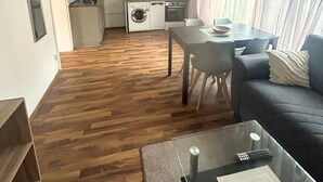 A modern living room with a wooden floor, a sofa, a dining table, and a kitchen area in the background. - Stadtnahe Wohnung mit Küche - Ideal für Familien, Singles und Geschäftsreisende! (Oelde)