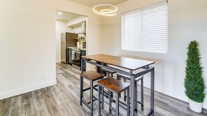 A modern kitchen with a wooden table and bar stools, a potted plant, and a window with blinds. - Cozy Couple's Condo! Walk to Old Town Scottsdale (Scottsdale)