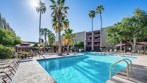 A swimming pool with lounge chairs and umbrellas, surrounded by palm trees and a multi-story building. - Cozy Couple's Condo! Walk to Old Town Scottsdale (Scottsdale)
