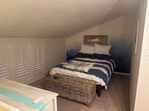 A bedroom with a bed, a wicker bench, a dresser, and a wall-mounted shelf.