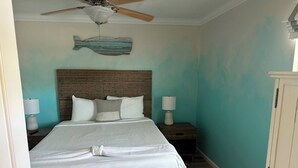 A bedroom with a bed, two bedside lamps, a ceiling fan, a wooden headboard, and a wall-mounted fish decoration. - 10F, Wave Hello (Miramar Beach)