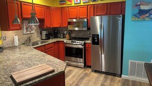 A kitchen with red cabinets, stainless steel appliances, and a granite countertop. - 10F, Wave Hello (Miramar Beach)