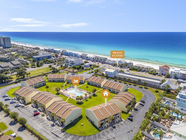 An aerial view of a resort with a central pool, beach access, and a view of the ocean.