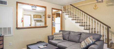 A living room with a gray sectional sofa, a coffee table, and a staircase with a wooden railing.