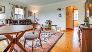 A living room with a brown leather sofa, a wooden dining table with four chairs, a patterned rug, and a hallway leading to another room.