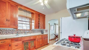 A kitchen with wooden cabinets, a tiled backsplash, a gas stove, and a window with blinds.