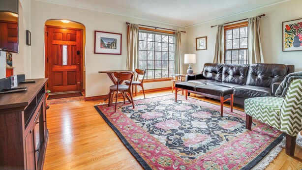 A living room with a wooden floor, a leather sofa, a patterned rug, and a dining area with chairs and a table.