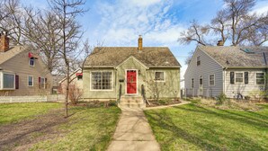 A single-story house with a red front door, a visible chimney, and a white picket fence in the background.