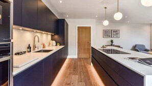 A modern kitchen with dark cabinetry, a central island, and pendant lighting. - Luxury Chichester Home for 12 (West Sussex)