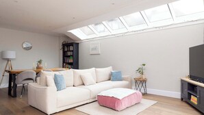 A living room with a sofa, ottoman, and a TV stand. - Luxury Chichester Home for 12 (West Sussex)