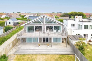 Et moderne hus med en stor balkon, en overdækket terrasse og udsigt til omkringliggende huse.