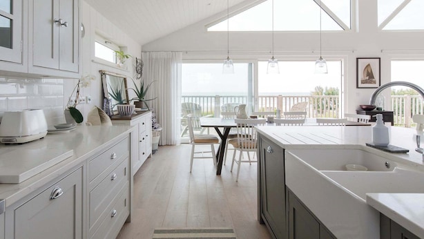 Una cocina con una isla grande, muebles blancos y una zona de comedor con mesa y sillas.