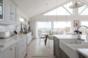 A kitchen with a large island, white cabinetry, and a dining area with a table and chairs. - Hamptons Style Lux Beach house (Bracklesham Bay)